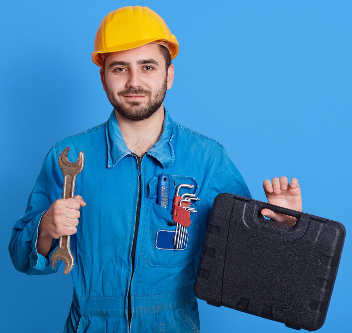 young handsome repairman blue overall yellow helmet holding toolbox wrench bearded plumber standing isolated color wall man working holds toolbox with instrument e1691965162461
